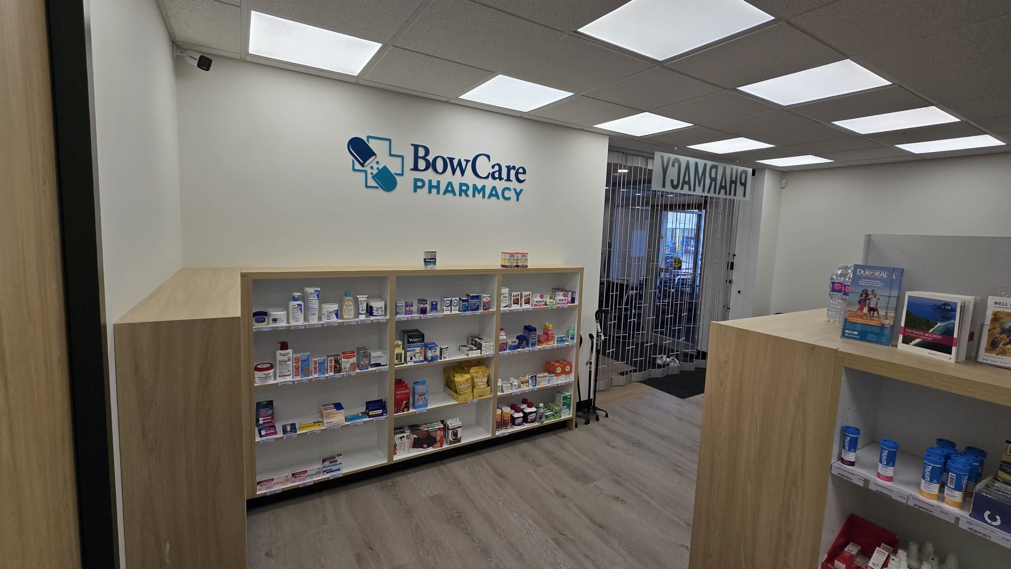 Bow Care Pharmacy OTC product wall beneath illuminated logo sign