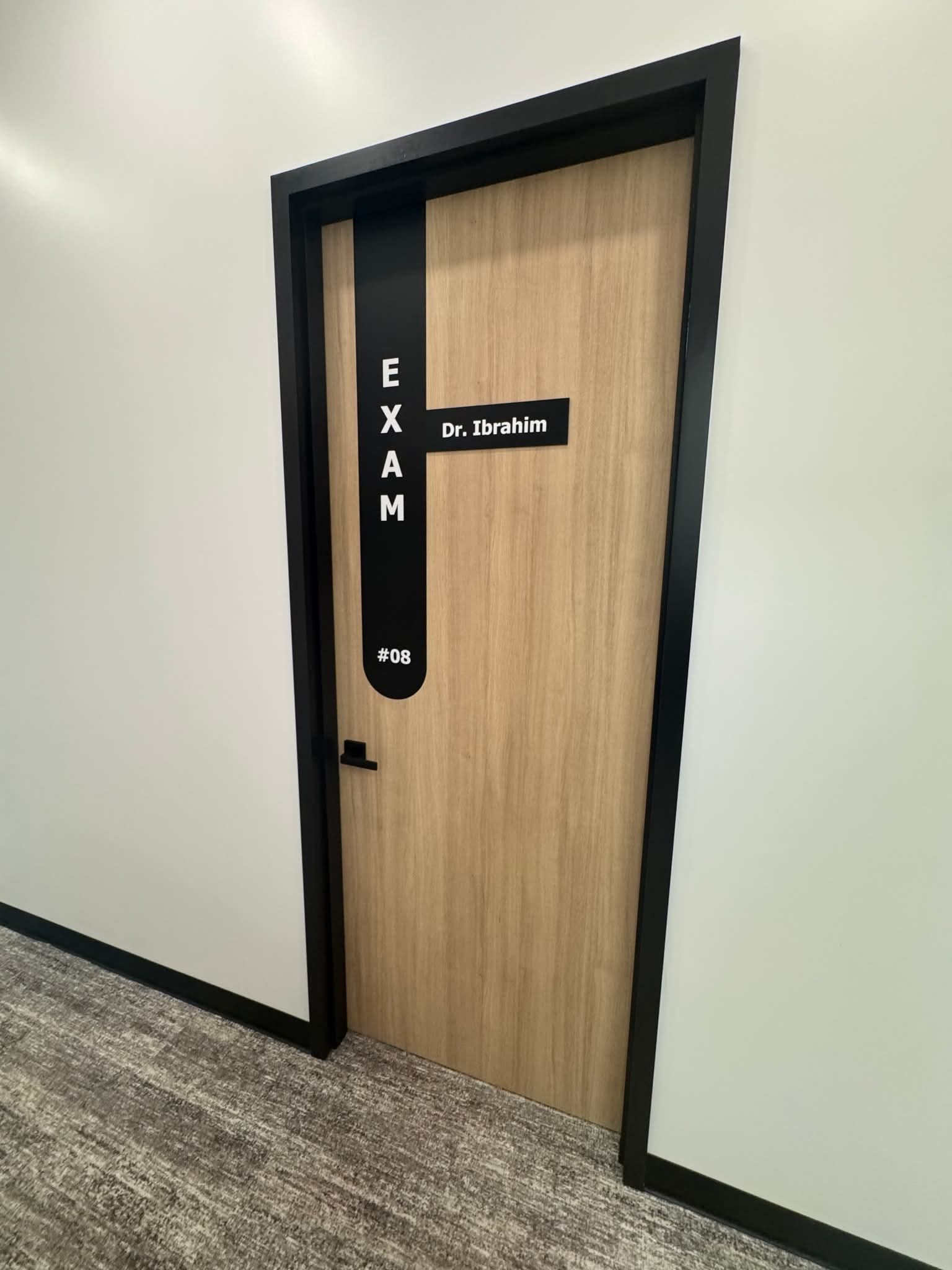 Physician's consult room with desk, exam table, and wall-mounted vitals equipment